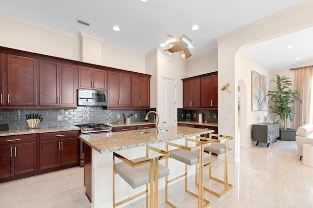 kitchen with stainless steel appliances, a sink, backsplash, light stone counters, and ornamental molding