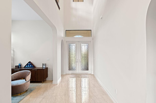 entrance foyer with arched walkways, a towering ceiling, baseboards, and french doors