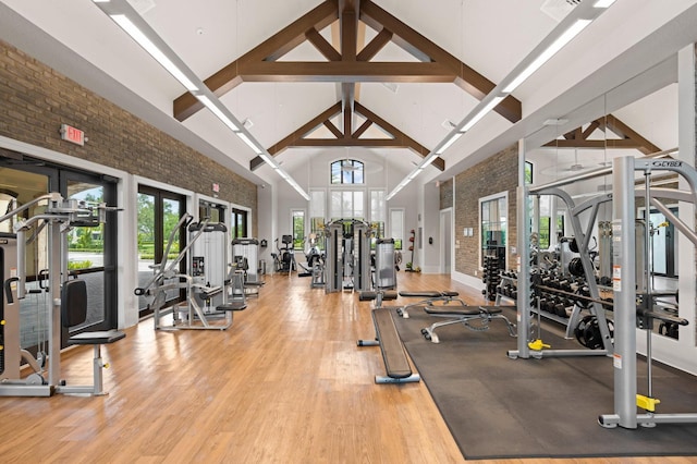 exercise room with high vaulted ceiling, brick wall, french doors, and wood finished floors