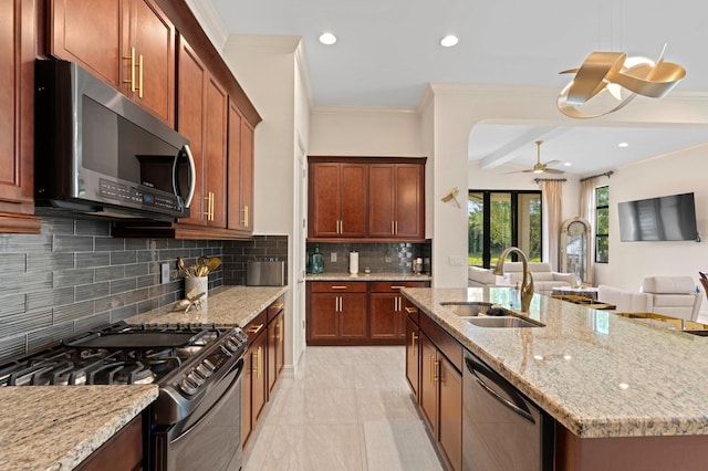 kitchen with a sink, open floor plan, a ceiling fan, light stone counters, and appliances with stainless steel finishes