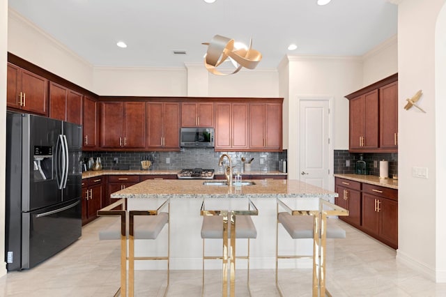kitchen with a sink, decorative backsplash, stainless steel microwave, refrigerator with ice dispenser, and light stone countertops