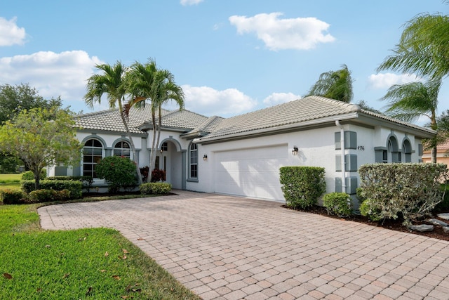 mediterranean / spanish house with stucco siding, driveway, a tiled roof, and an attached garage