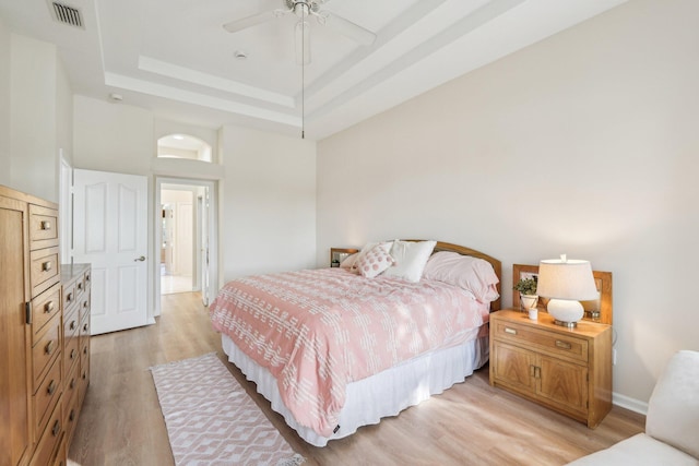 bedroom featuring a ceiling fan, visible vents, light wood-style flooring, and a tray ceiling