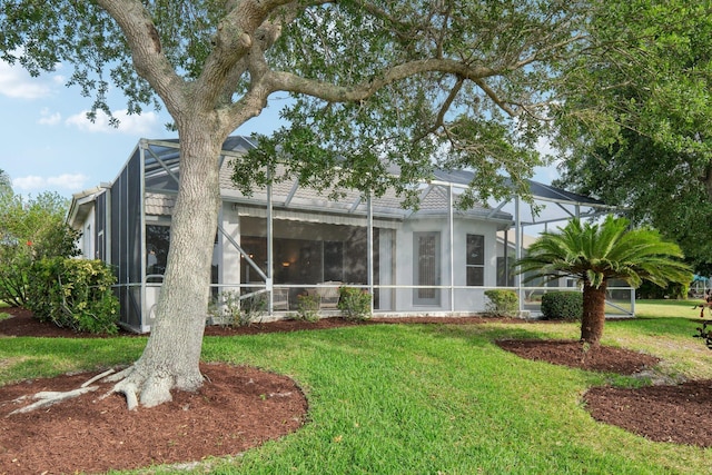 rear view of house with a lawn, stucco siding, and glass enclosure