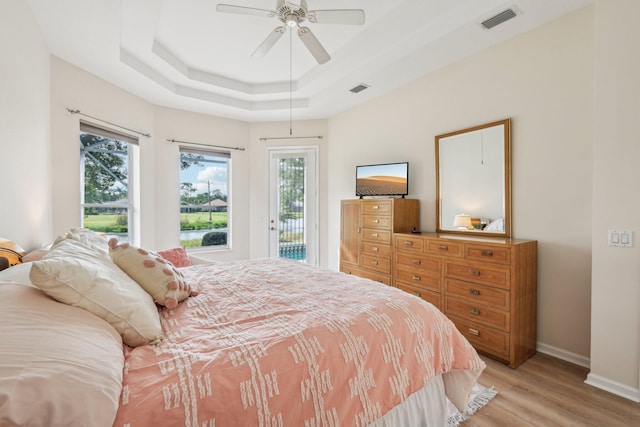 bedroom featuring visible vents, a tray ceiling, light wood finished floors, and access to exterior