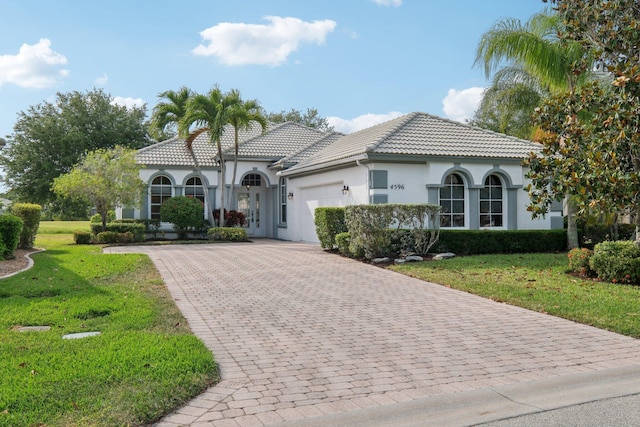 mediterranean / spanish house featuring a front lawn, stucco siding, driveway, and an attached garage