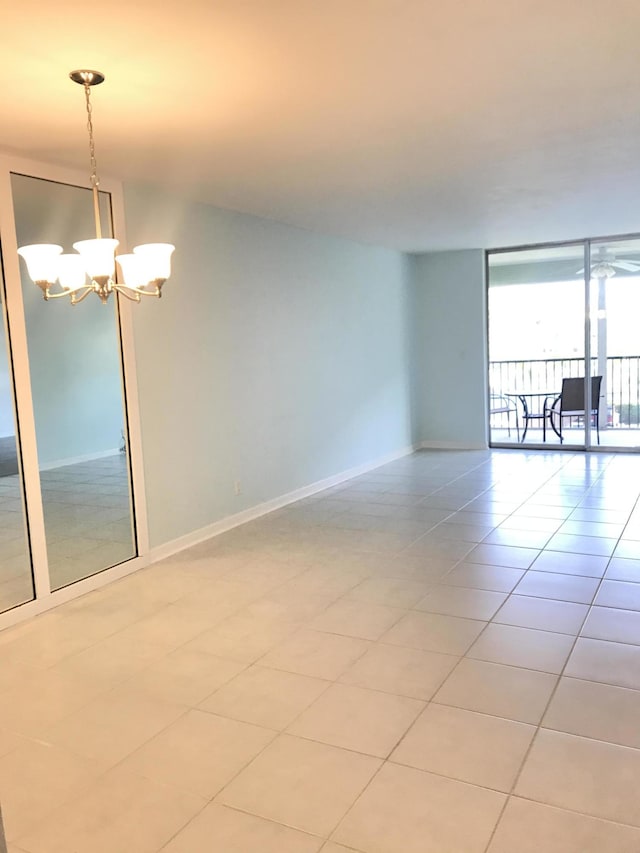 empty room with baseboards, an inviting chandelier, a wall of windows, and light tile patterned floors