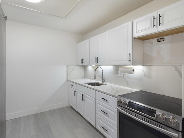 kitchen with light stone counters, electric stove, a sink, light wood finished floors, and white cabinets