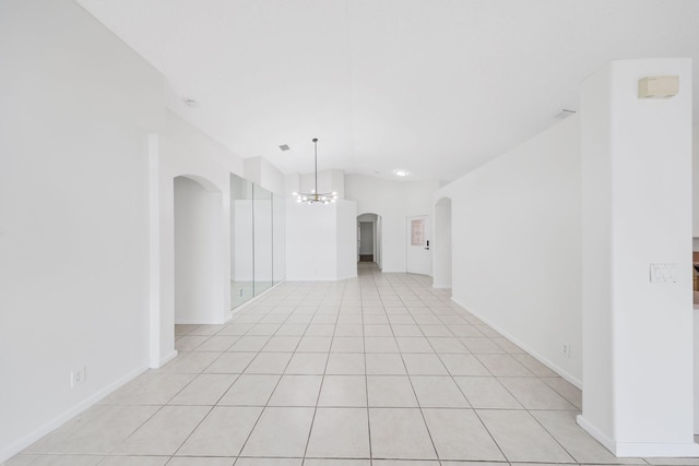 unfurnished room with baseboards, arched walkways, a notable chandelier, vaulted ceiling, and light tile patterned flooring