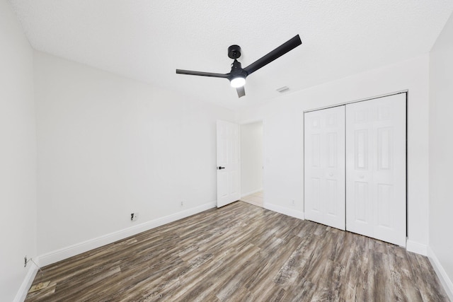 unfurnished bedroom featuring visible vents, a closet, baseboards, ceiling fan, and wood finished floors