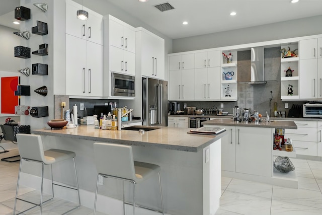 kitchen with wall chimney range hood, open shelves, stainless steel appliances, a peninsula, and visible vents