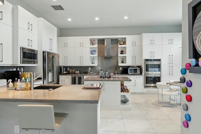 kitchen with wall chimney exhaust hood, stainless steel appliances, wine cooler, a sink, and visible vents