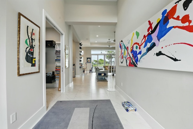 hallway featuring baseboards, a tray ceiling, and recessed lighting