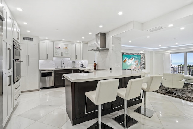 kitchen featuring stainless steel appliances, a peninsula, a sink, visible vents, and wall chimney range hood