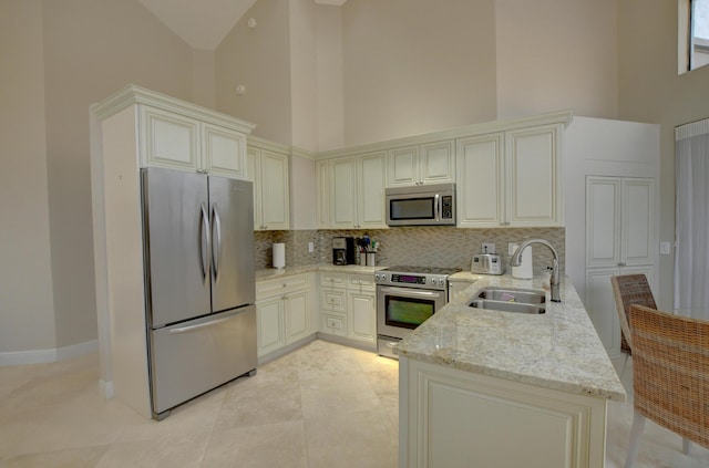 kitchen featuring high vaulted ceiling, a sink, backsplash, appliances with stainless steel finishes, and light stone countertops