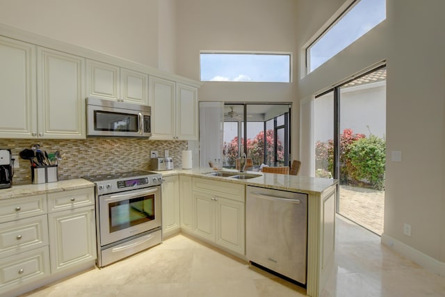 kitchen with stainless steel appliances, a sink, tasteful backsplash, a high ceiling, and light stone countertops