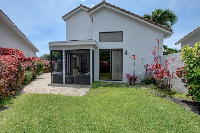 rear view of property with a tiled roof, a lawn, a sunroom, a patio, and stucco siding