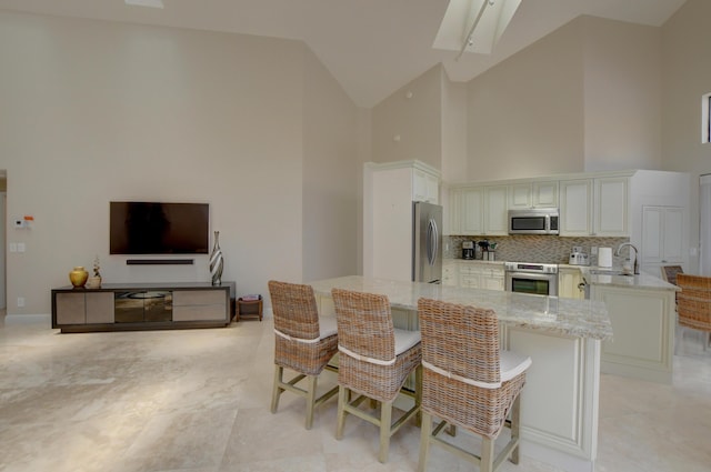 kitchen with a kitchen breakfast bar, light stone counters, a peninsula, appliances with stainless steel finishes, and high vaulted ceiling