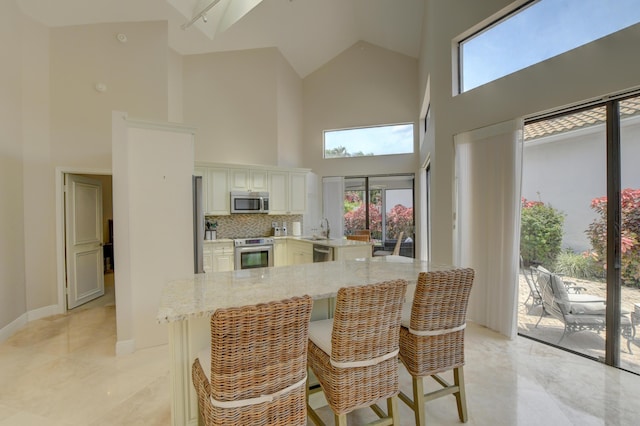 kitchen with high vaulted ceiling, a wealth of natural light, appliances with stainless steel finishes, and light stone countertops