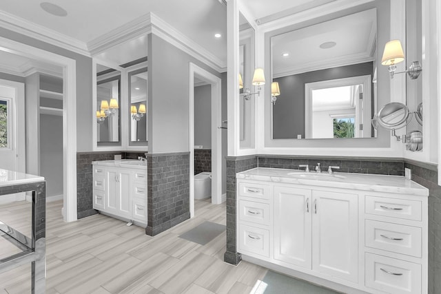 bathroom with wainscoting, two vanities, a sink, and tile walls
