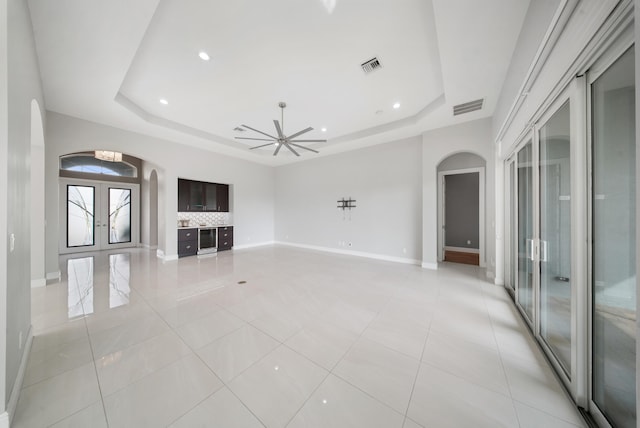 unfurnished living room featuring arched walkways, baseboards, visible vents, a raised ceiling, and french doors