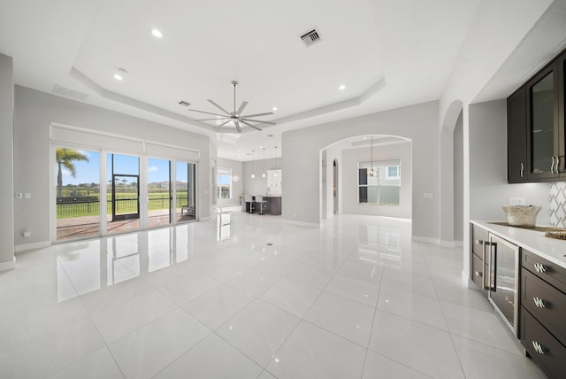 unfurnished living room with visible vents, arched walkways, ceiling fan, and a raised ceiling