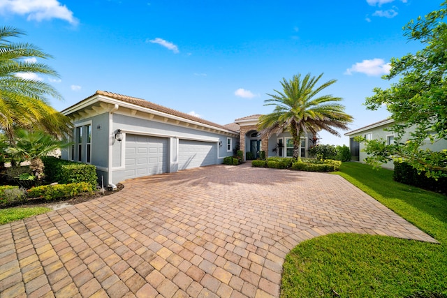 mediterranean / spanish home with stucco siding, decorative driveway, a garage, a tile roof, and a front lawn