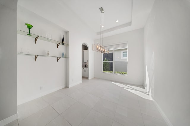 unfurnished dining area featuring light tile patterned flooring, arched walkways, a notable chandelier, and baseboards