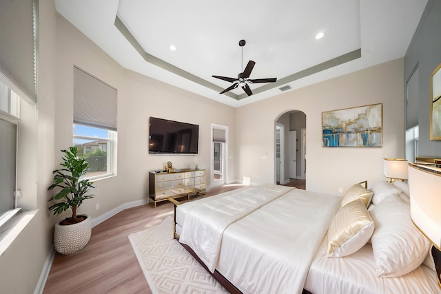 bedroom with light wood-style floors, a tray ceiling, visible vents, baseboards, and arched walkways