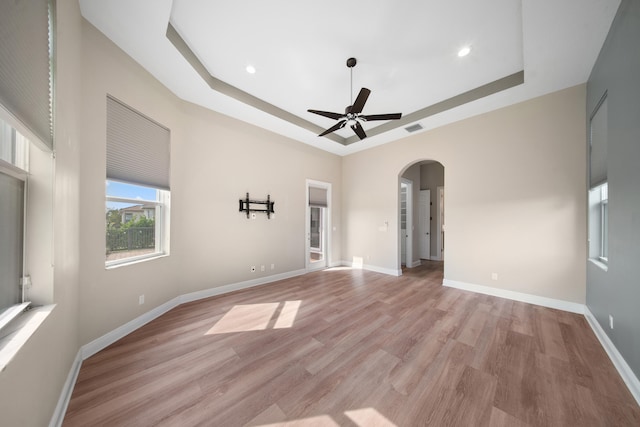 spare room featuring light wood finished floors, ceiling fan, a tray ceiling, visible vents, and arched walkways