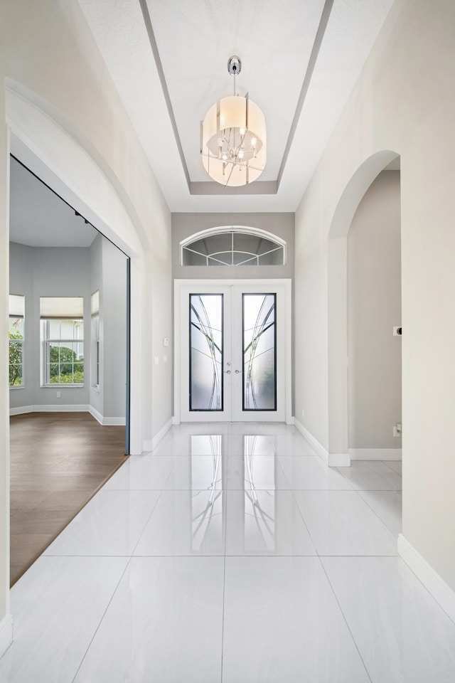 foyer entrance with arched walkways, french doors, a chandelier, and baseboards