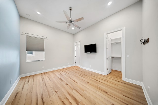 unfurnished bedroom with recessed lighting, a walk in closet, wood finished floors, and baseboards