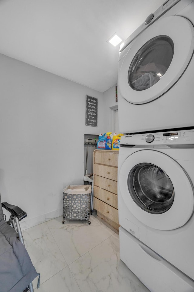 laundry room with stacked washer / drying machine, baseboards, marble finish floor, and laundry area