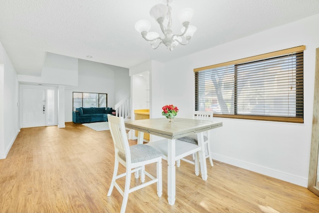 dining space with light wood-style floors, a textured ceiling, baseboards, and an inviting chandelier
