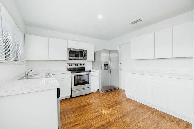 kitchen featuring stainless steel appliances, light countertops, visible vents, a sink, and light wood-type flooring