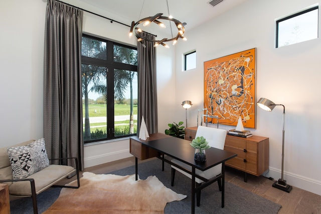 home office with baseboards, wood finished floors, a towering ceiling, and a chandelier