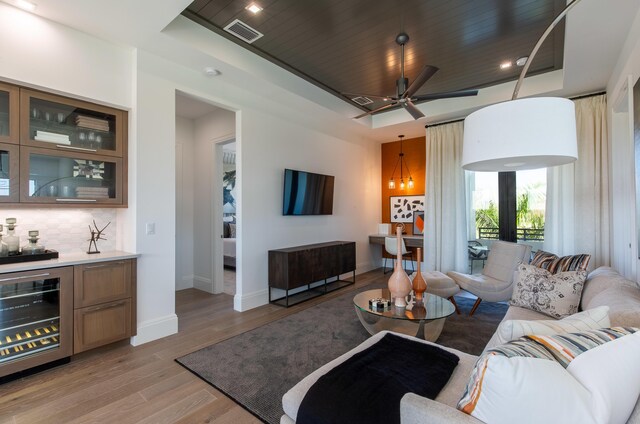 living area featuring wine cooler, a tray ceiling, light wood-type flooring, visible vents, and baseboards
