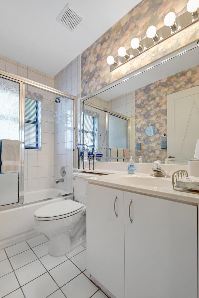 bathroom featuring bath / shower combo with glass door, visible vents, wallpapered walls, toilet, and vanity
