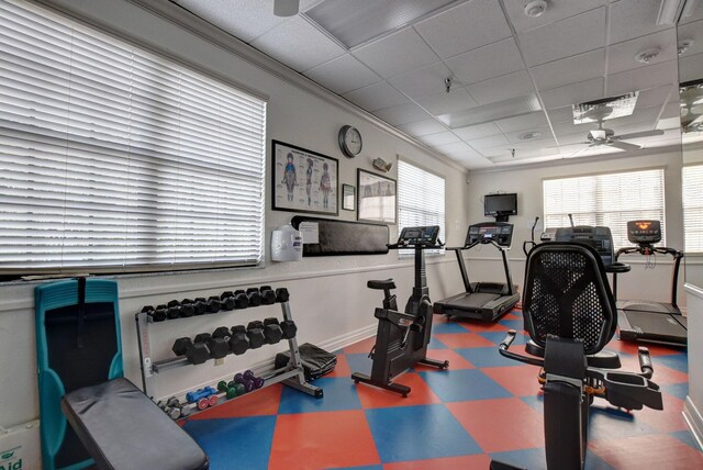 exercise room with a paneled ceiling, ceiling fan, and baseboards