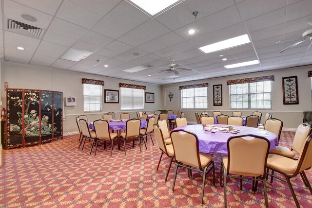 carpeted dining area with visible vents, ceiling fan, a drop ceiling, and baseboards