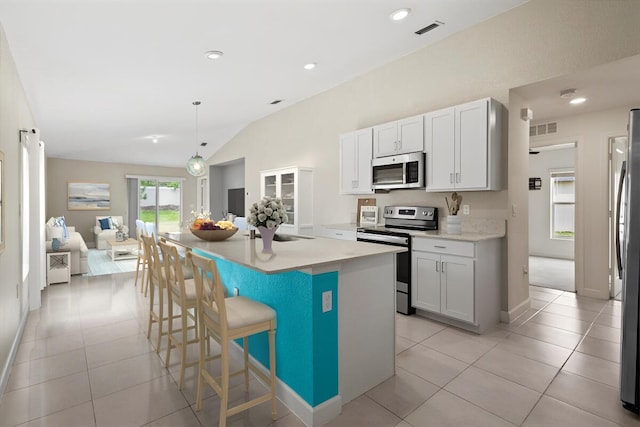 kitchen with appliances with stainless steel finishes, lofted ceiling, open floor plan, light tile patterned flooring, and a kitchen breakfast bar
