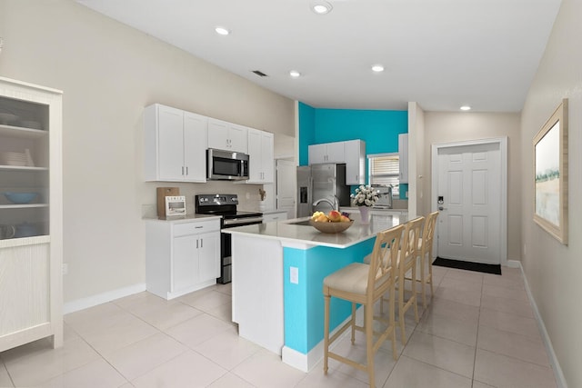 kitchen featuring stainless steel appliances, a kitchen breakfast bar, white cabinets, a center island with sink, and light tile patterned floors
