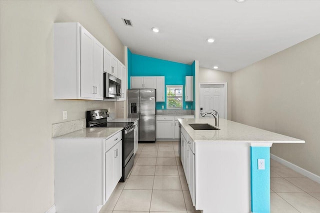 kitchen featuring stainless steel appliances, a sink, vaulted ceiling, an island with sink, and white cabinets