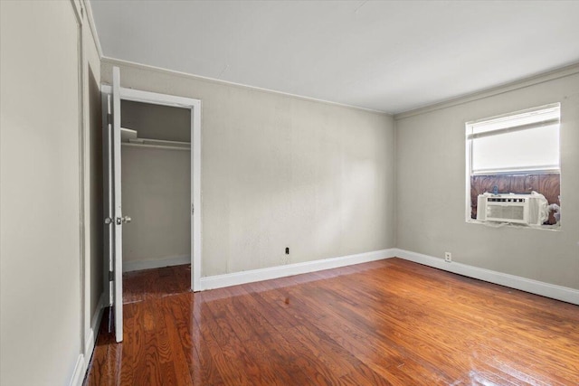 unfurnished bedroom with cooling unit, baseboards, wood finished floors, a closet, and a walk in closet