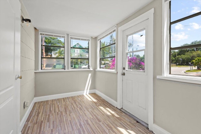 unfurnished sunroom featuring baseboards, a healthy amount of sunlight, and wood finished floors