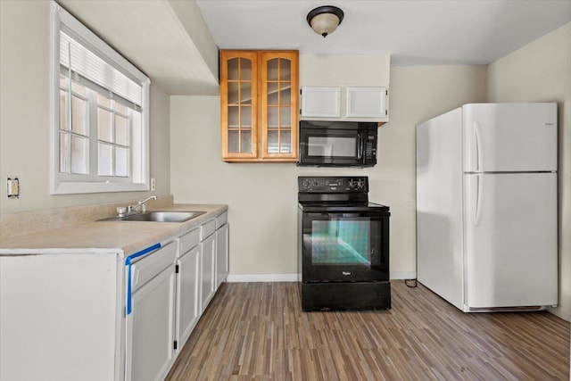 kitchen with white cabinets, wood finished floors, a sink, black appliances, and glass insert cabinets