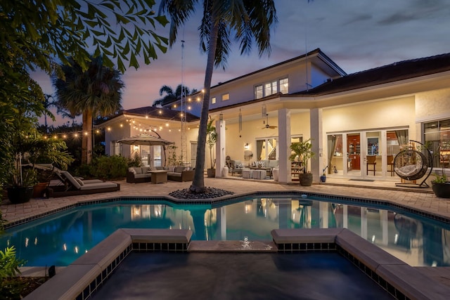 2409 NE 12th St, Fort Lauderdale, FL 33304 - back of property at dusk featuring outdoor lounge area, a patio area, ceiling fan, a pool with connected hot tub, and stucco siding