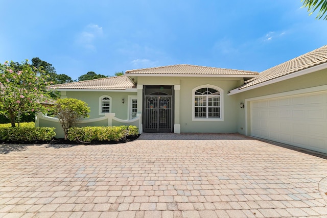 entrance to property featuring stucco siding, a tile roof, a garage, and decorative driveway
