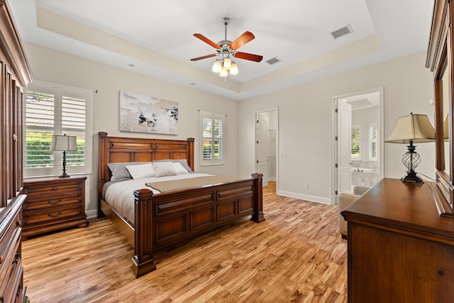 bedroom with light wood-type flooring, baseboards, a tray ceiling, and visible vents