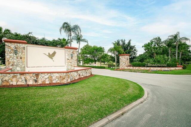 community / neighborhood sign with a lawn and curved driveway